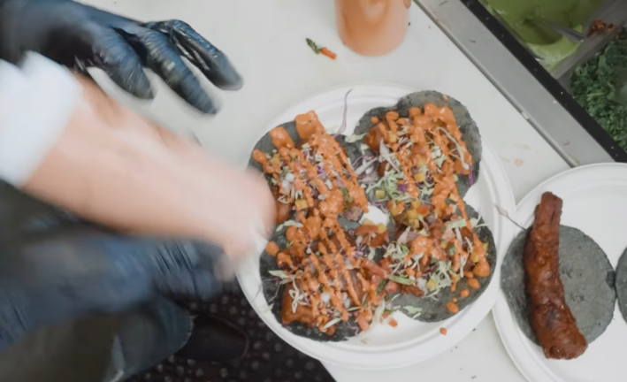 Fish tacos getting salsa poured on them.